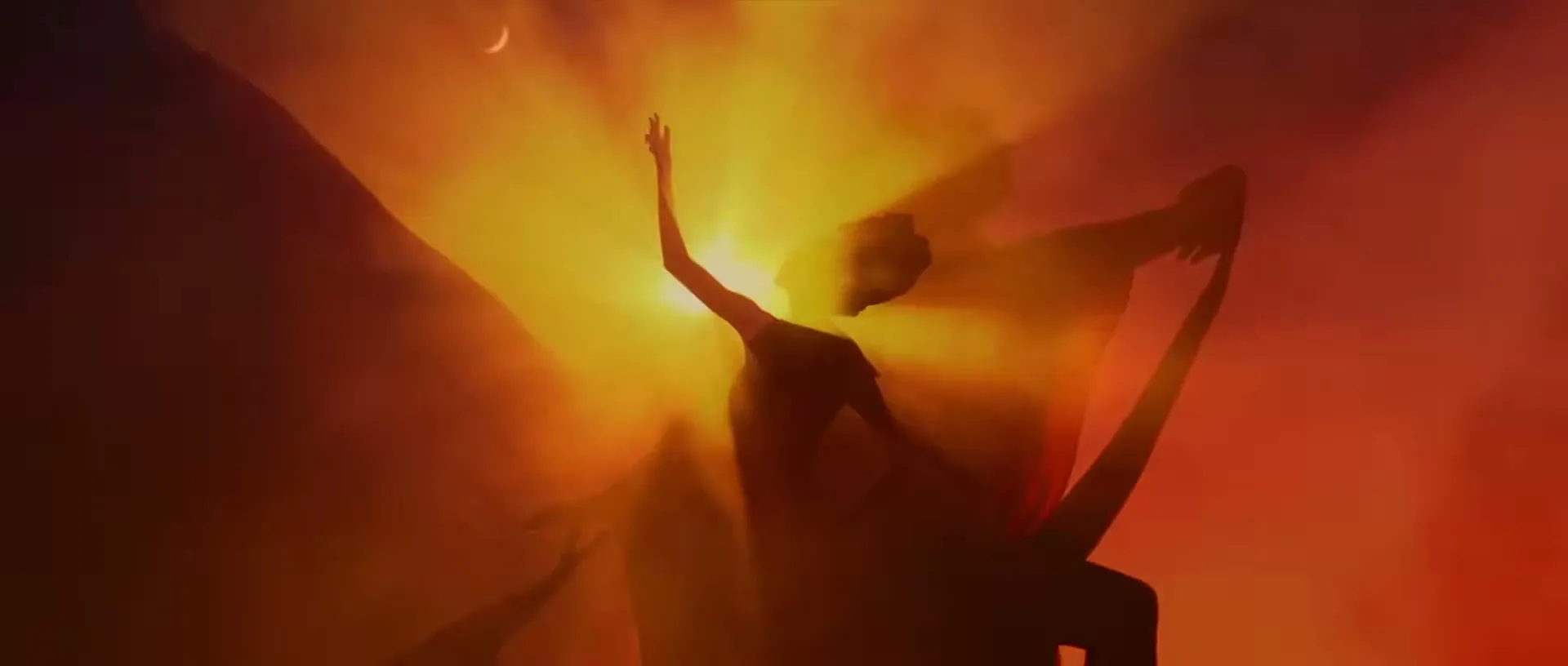 A female dancer in silhouette, with long hair, performs a dramatic pose against a vibrant orange and red sky with a crescent moon.