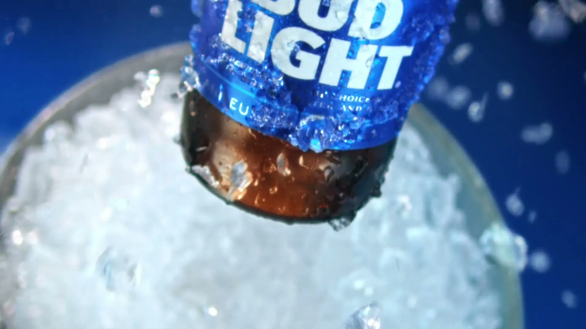 A Bud Light bottle, covered in condensation and ice, is pulled from a bucket of ice against a blue background.