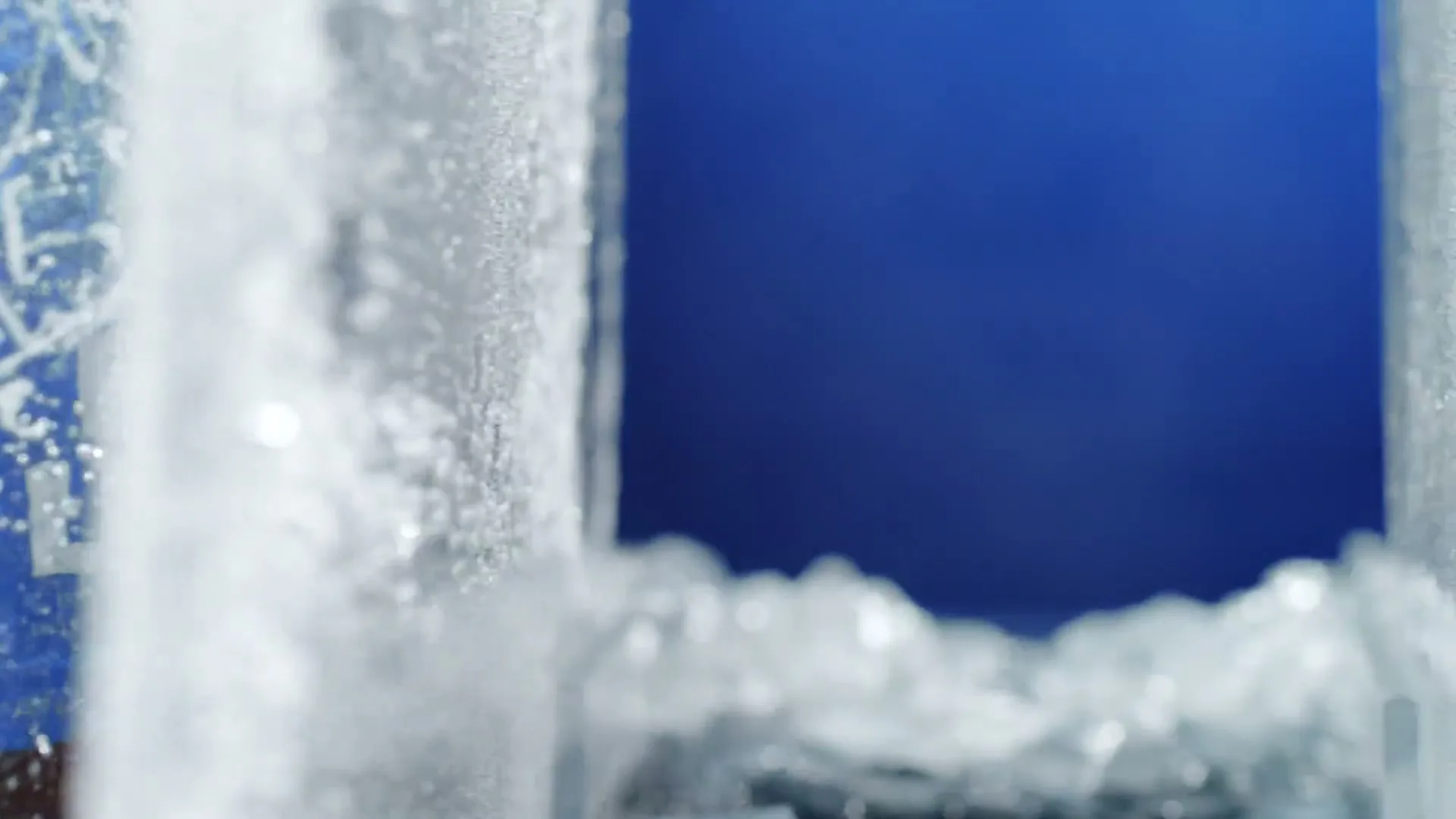 A close-up shot shows a block of ice shattering into many pieces against a blue background, creating a dynamic and refreshing visual.
