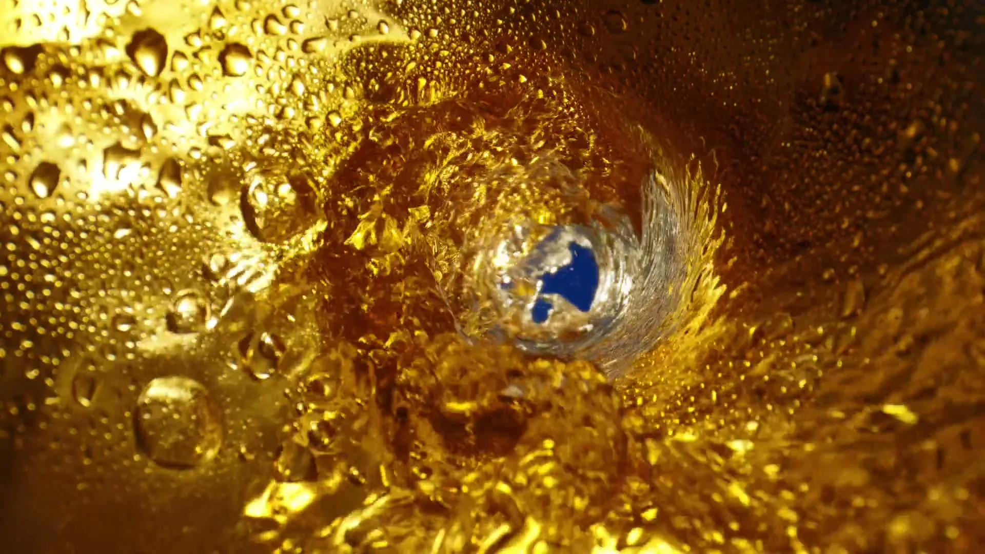 A close-up shot of golden liquid swirling down a drain, with condensation visible on the surrounding surface.