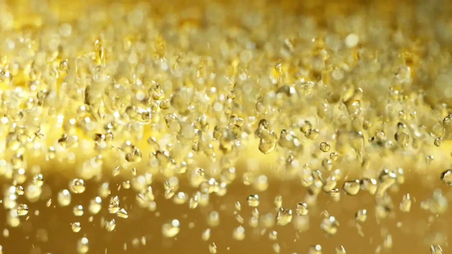 A close-up shot shows numerous golden bubbles rising and falling in a sparkling, effervescent liquid, creating a dynamic and refreshing visual.
