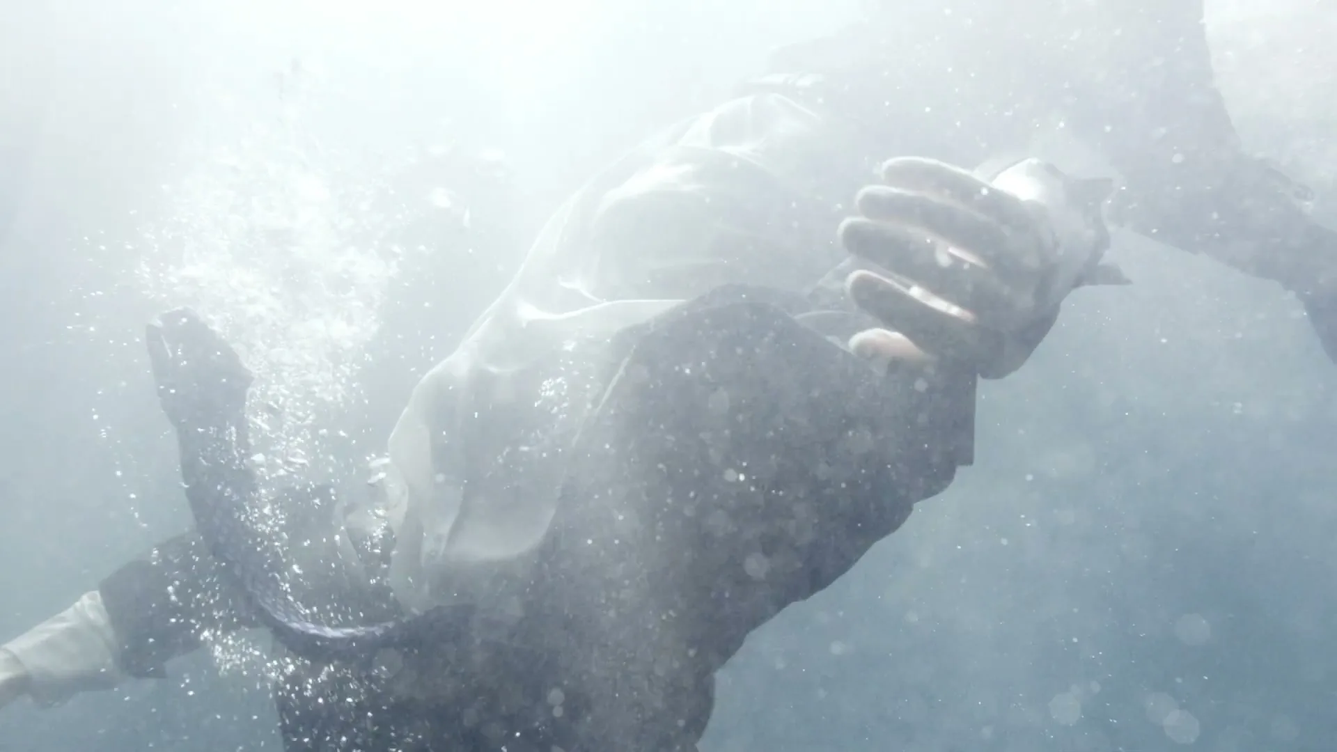 A person in dark clothes and a white shirt is seen underwater, with bubbles rising around them in a bright, hazy environment.