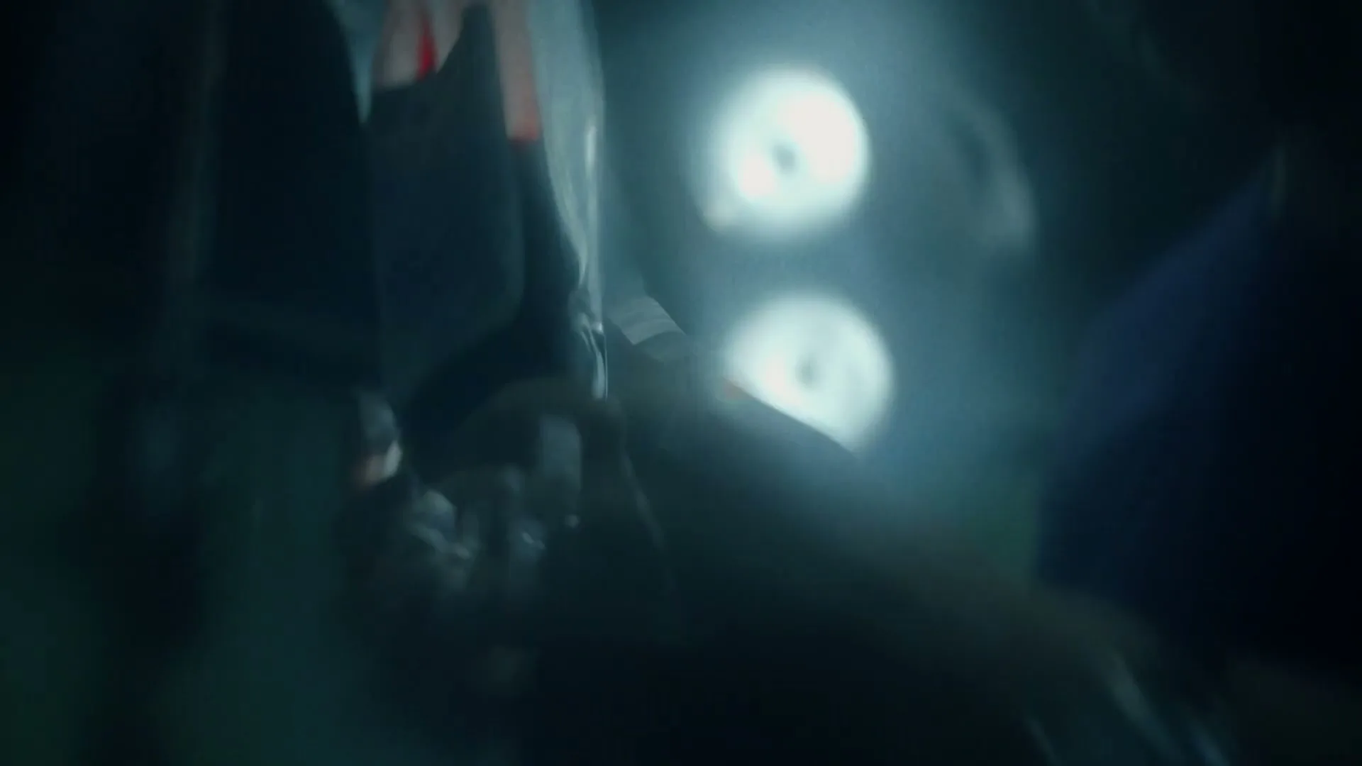 A surgeon in blue scrubs and cap is seen from a high angle, performing surgery in a dimly lit operating room.