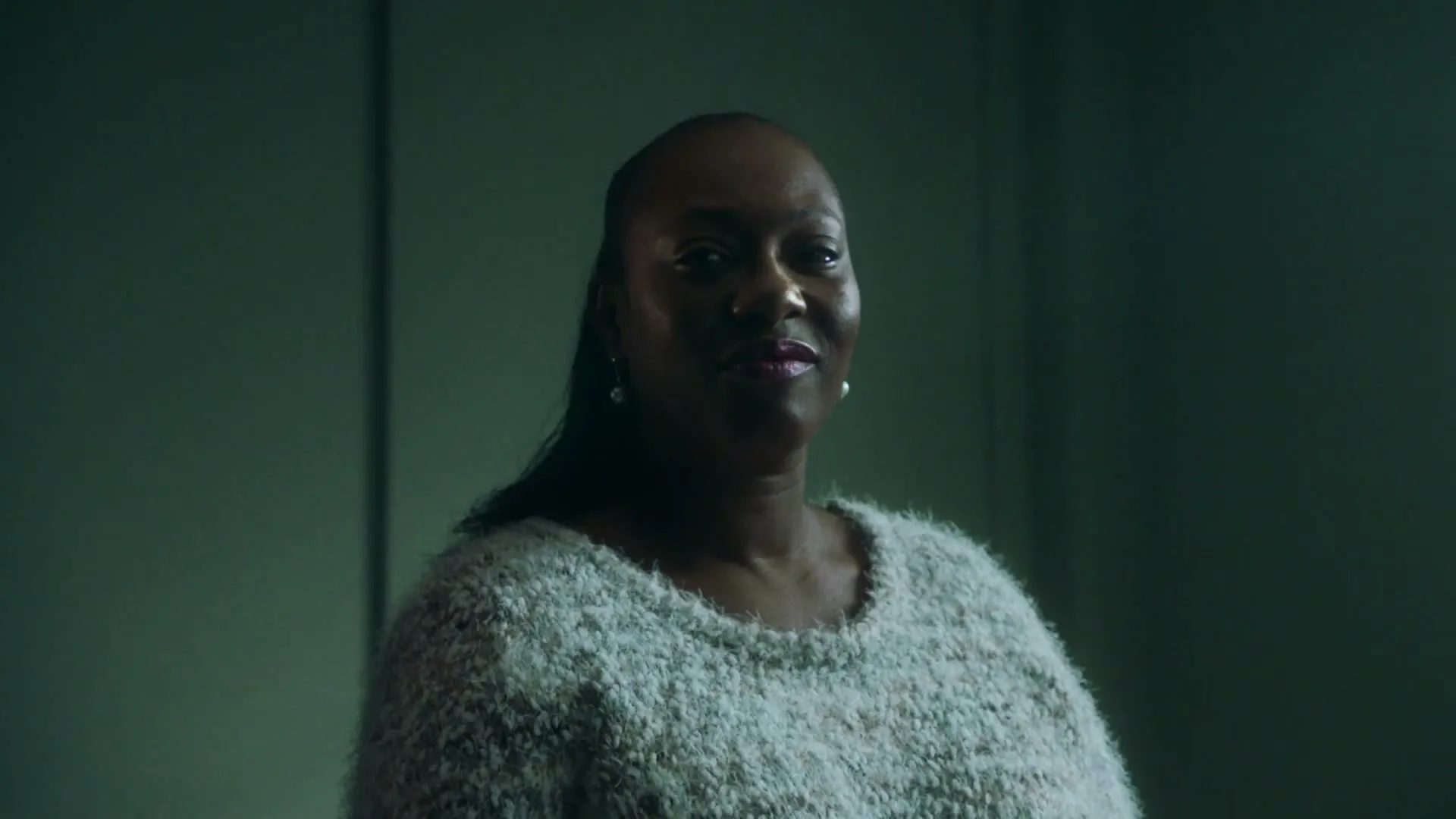 A Black woman in her 40s, wearing a light-colored fuzzy sweater, looks directly at the camera with a slight smile in an interior setting.
