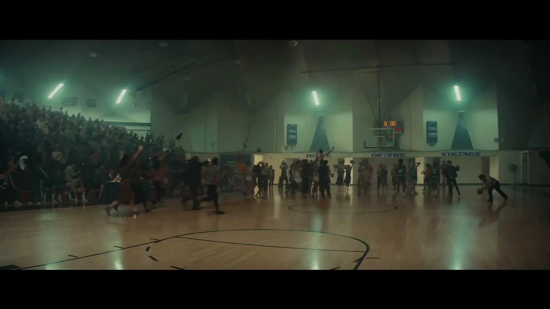 A wide shot of a high school basketball gym with a crowd cheering in the stands and players on the court.