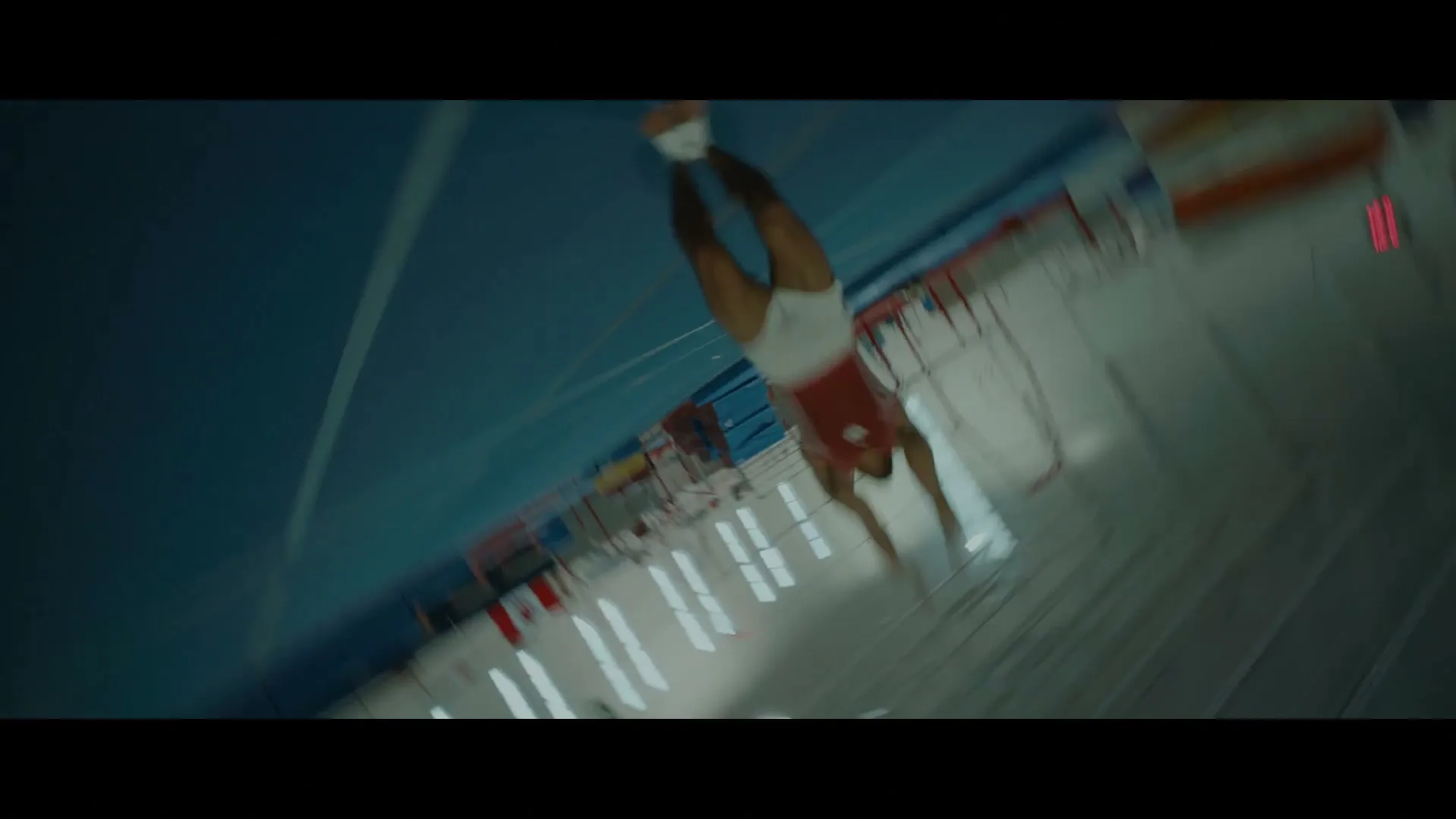A male gymnast in a red and white uniform performs a backflip on a trampoline in a brightly lit gymnasium.