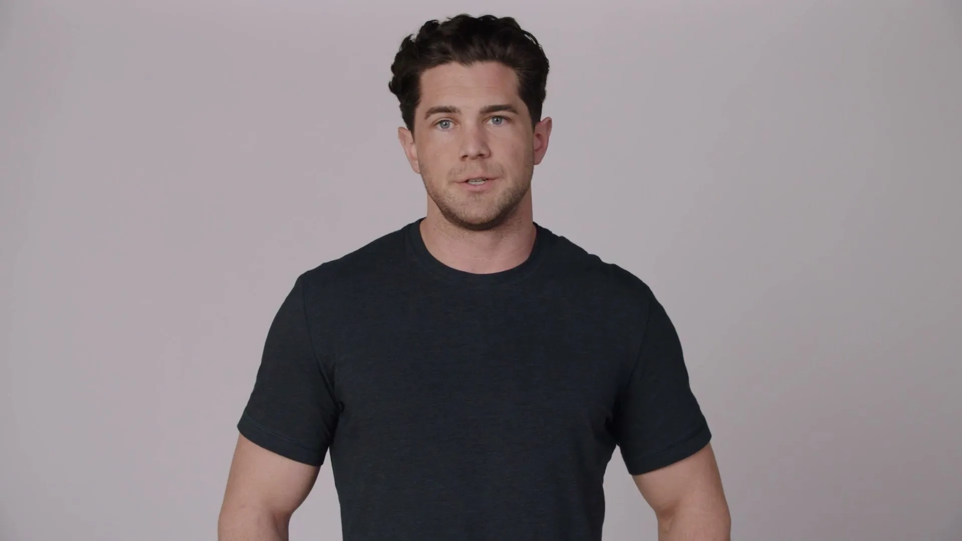 A young man with dark hair and a dark t-shirt stands in front of a plain white background, looking directly at the camera.