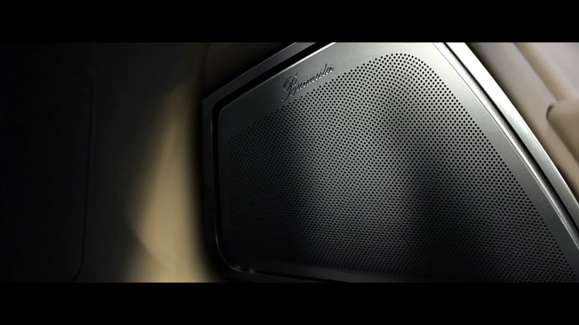 A close-up shot of a car speaker with a metallic grille and a brand logo, showcasing the intricate design and quality of the audio system.