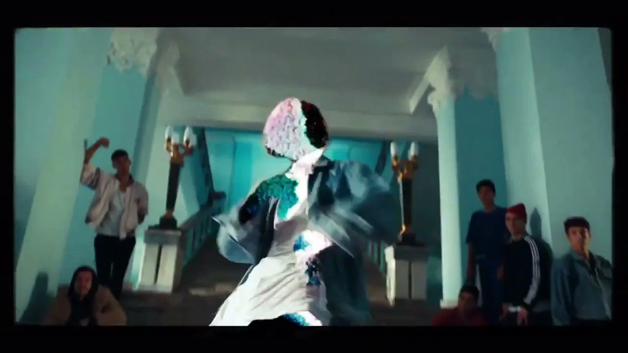 A young person with glitching skin and clothes dances in a grand hall with a group of young people watching.