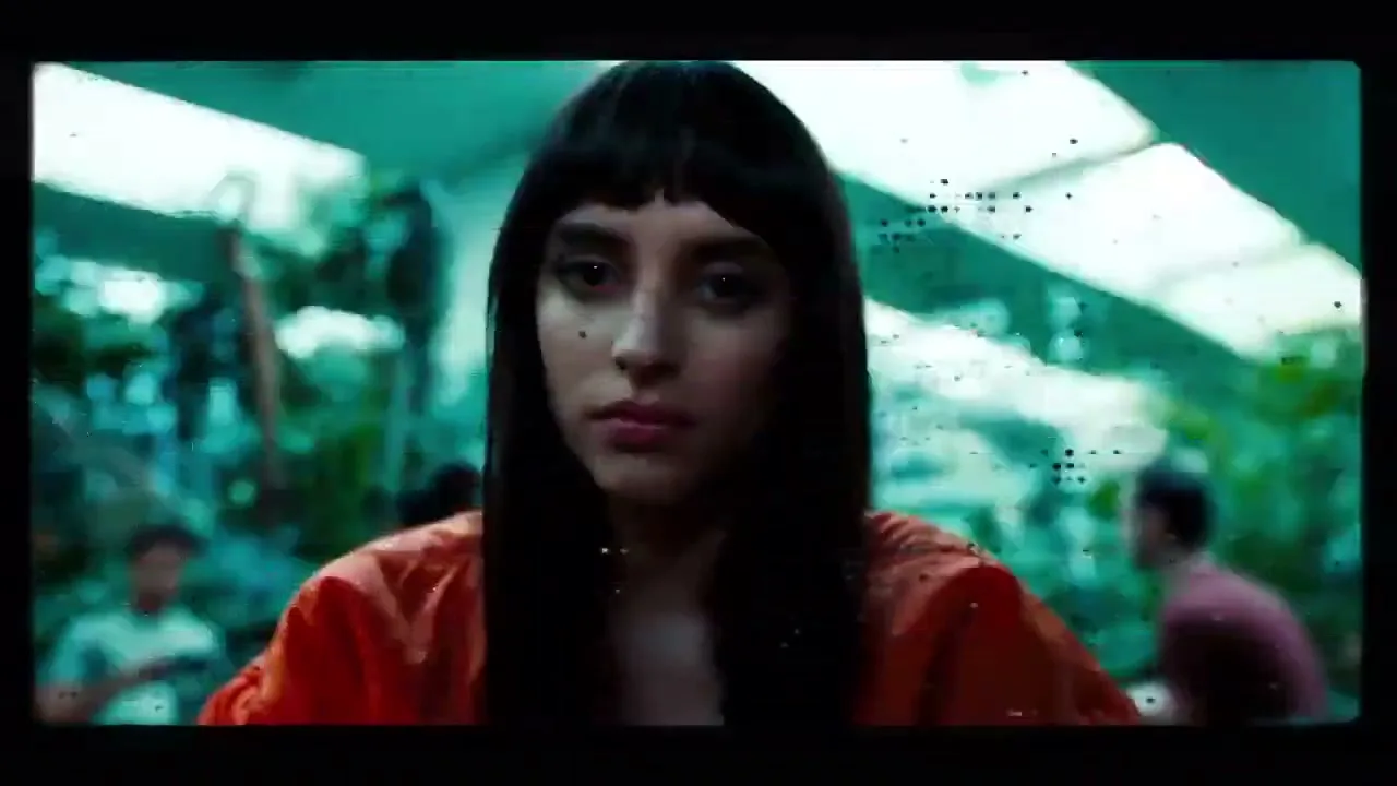 A young man's face is distorted by digital glitches, then transitions to a young woman with bangs and an orange top, also with digital glitches.