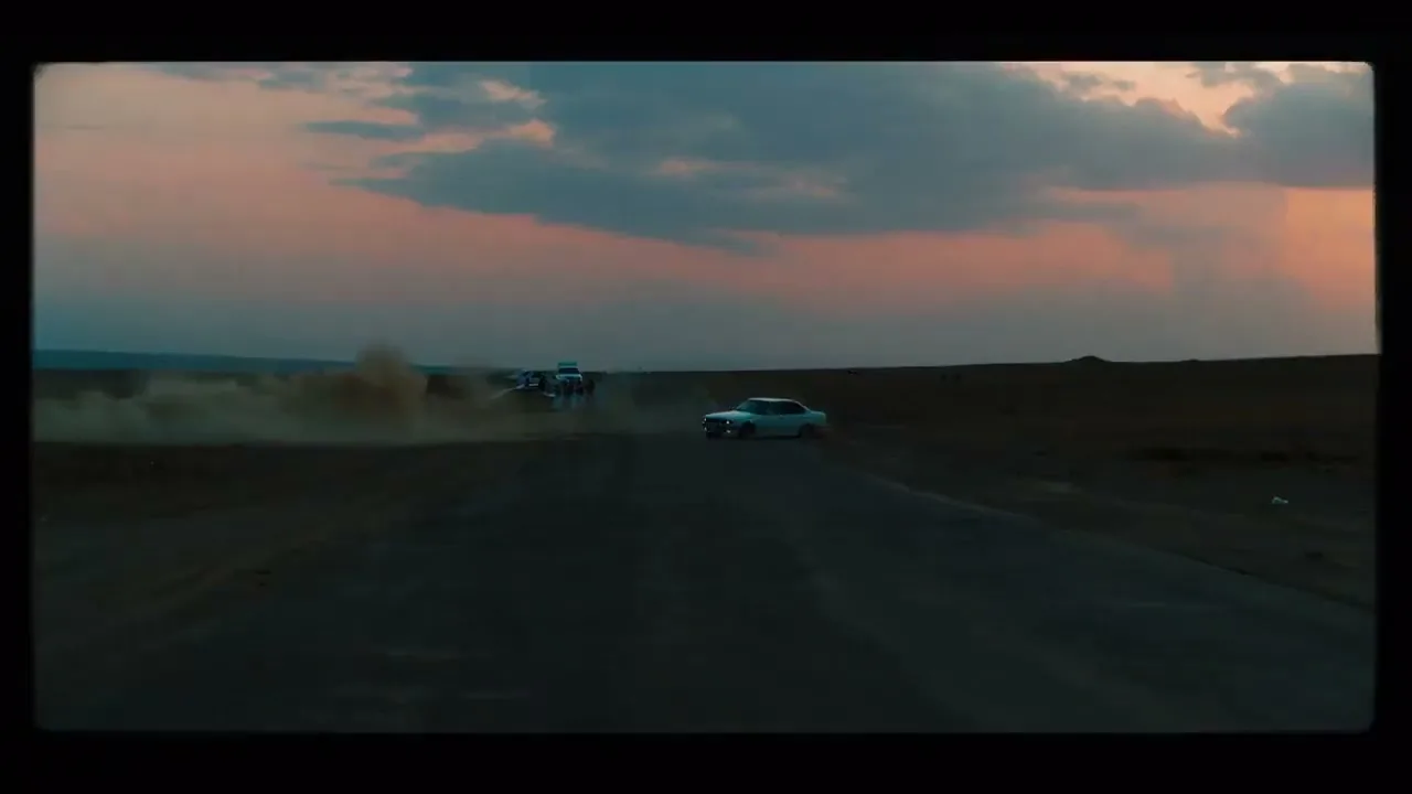 A white car drifts on a dirt road, kicking up dust, with a colorful sunset sky in the background.