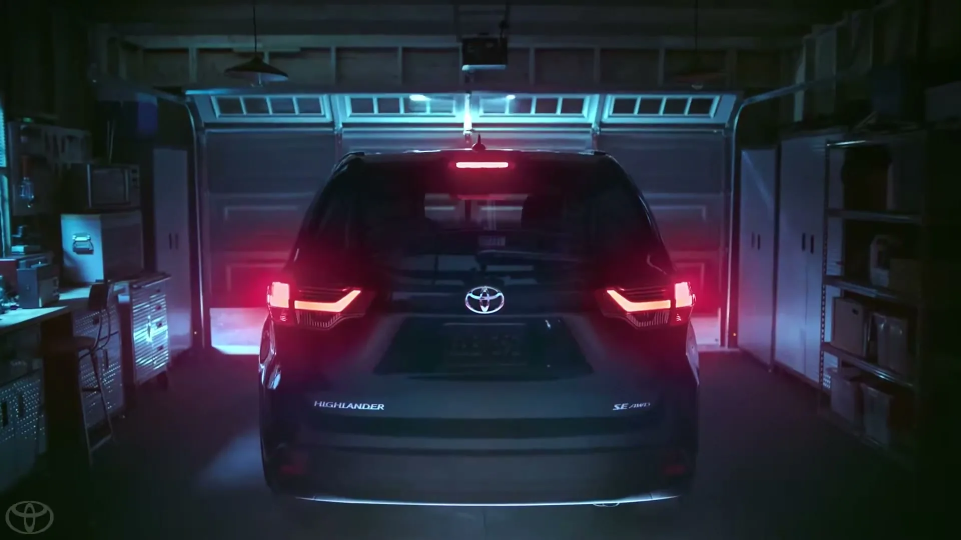 A dark blue Toyota Highlander SUV with its taillights on is parked in a dimly lit garage, facing away from the camera.