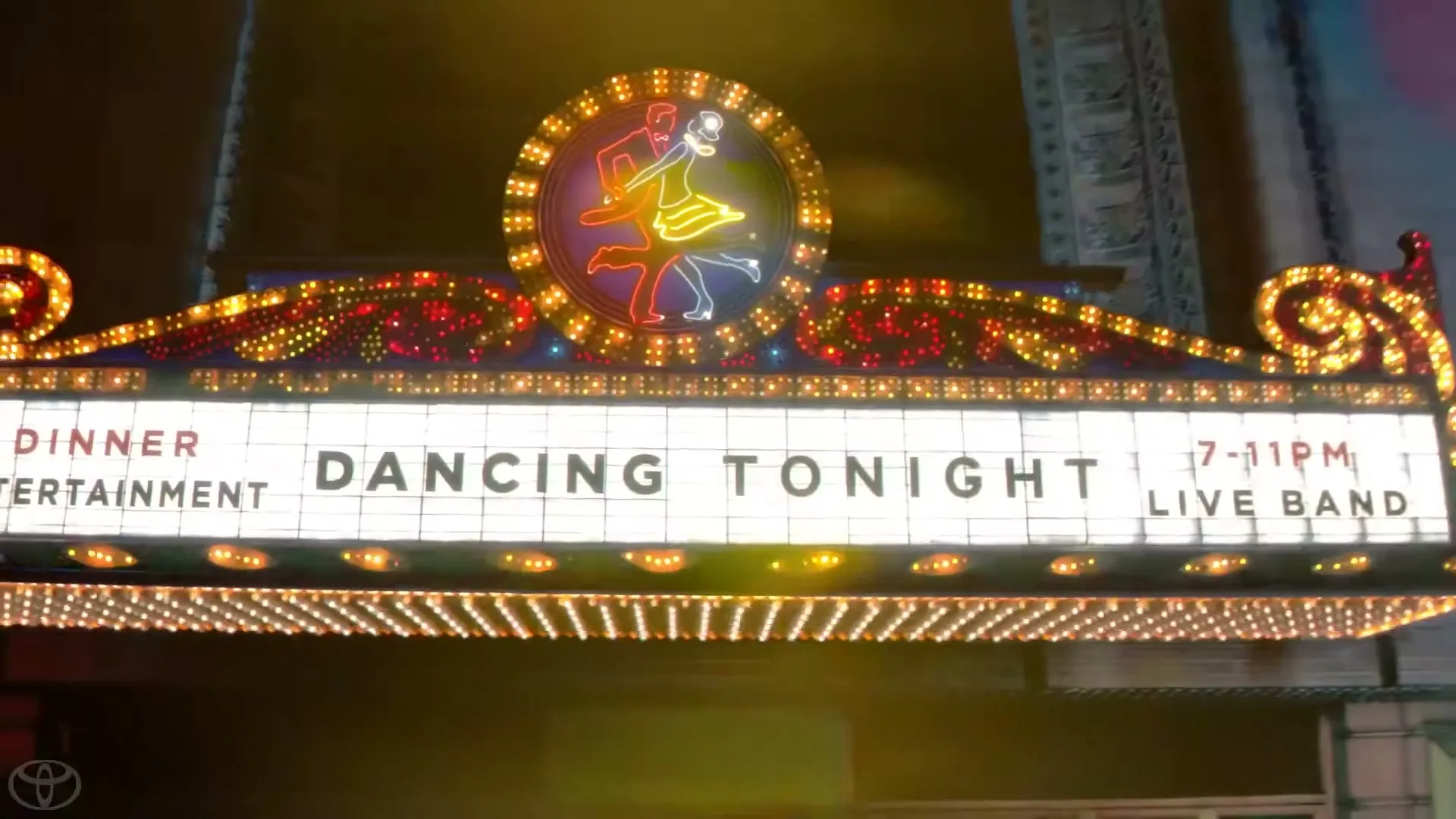 A brightly lit marquee sign for "DANCING TONIGHT" with a neon dancing couple, on a building at night.