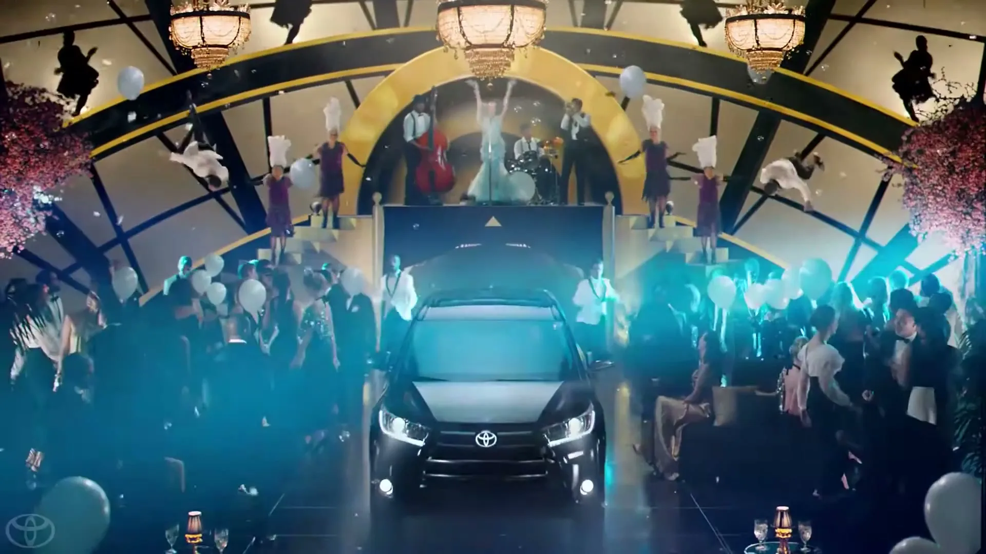 A black Toyota Highlander drives forward through a lavish, art deco-inspired party with many people dressed in formal attire, balloons, and confetti.