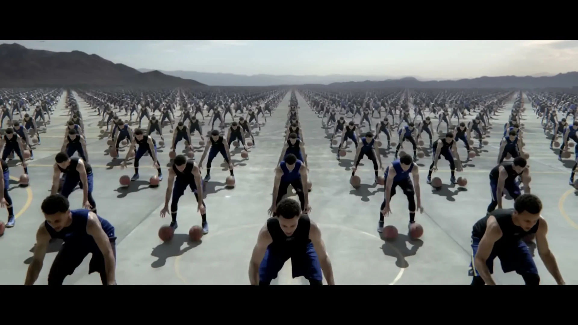 Hundreds of identical Stephen Curry clones in basketball uniforms dribble basketballs in unison on an endless outdoor court in a desert landscape.