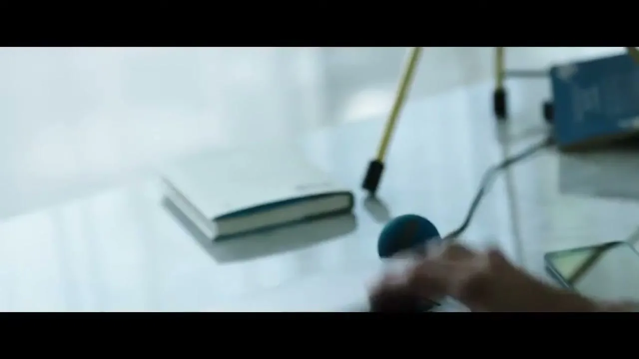 A man's hand closes a laptop on a desk in an interior setting during the day.