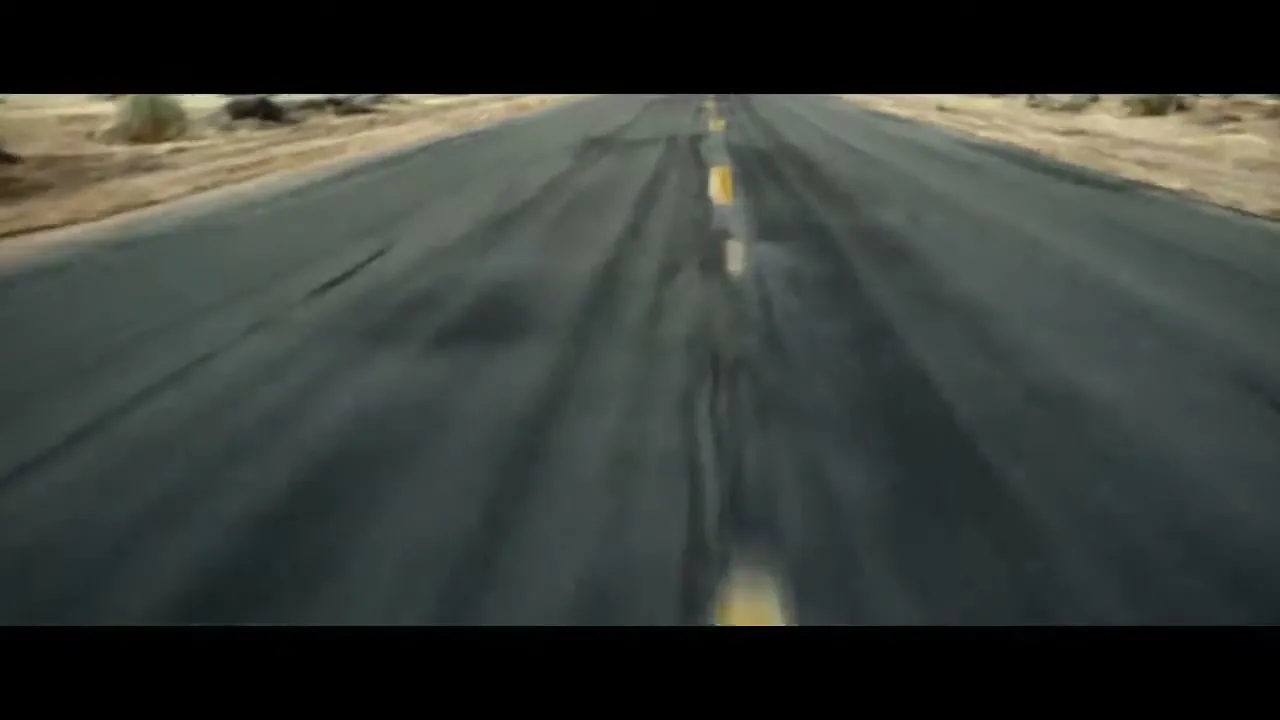 A low-angle shot of a long, empty desert road with a yellow dividing line, suggesting movement and travel.