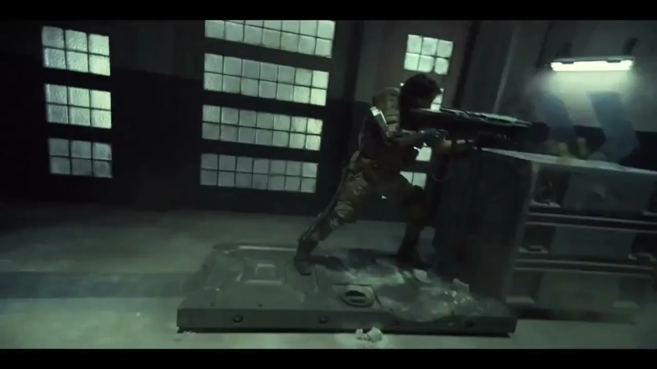 A male soldier in camouflage armor and holding a large weapon slides on a metal platform across a dark, industrial room with large windows.