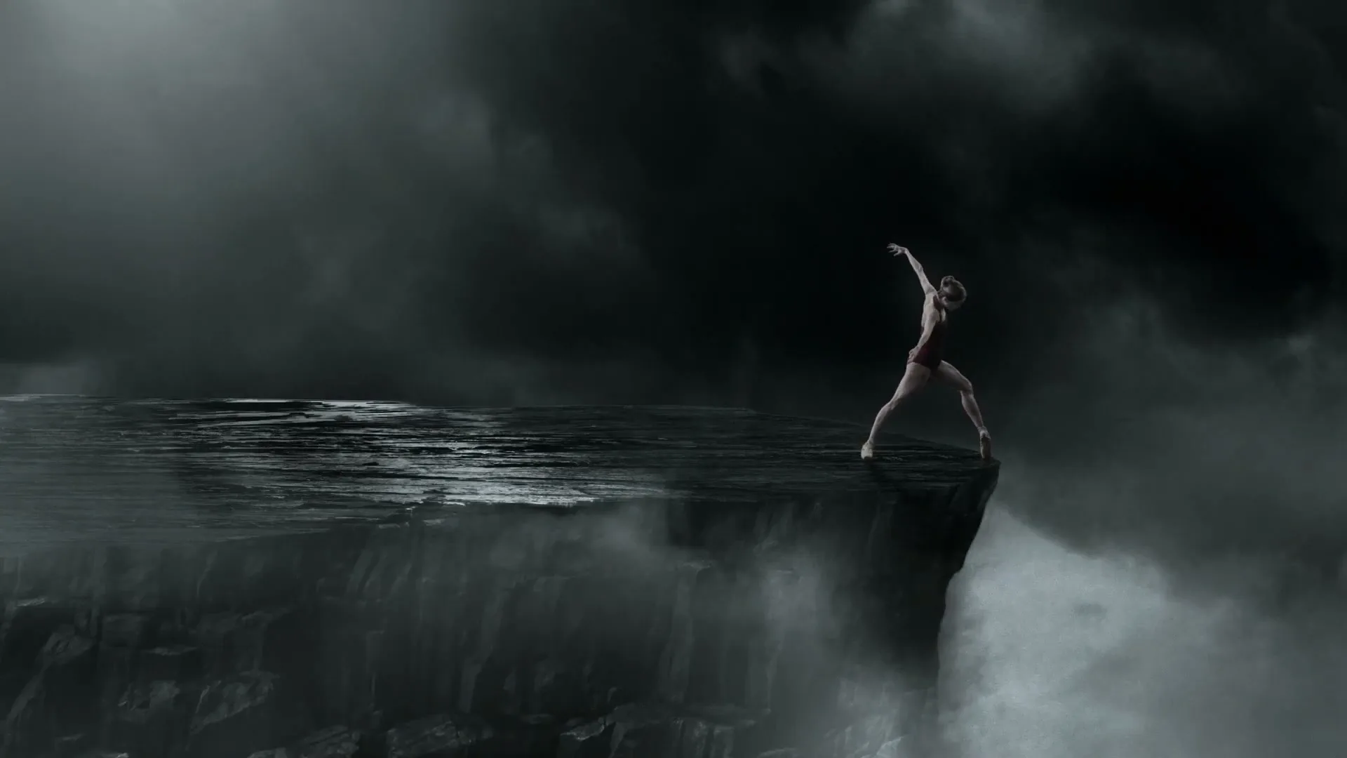 A female ballet dancer in a red leotard performs a pose on the edge of a cliff overlooking a waterfall, under a dark, cloudy sky.