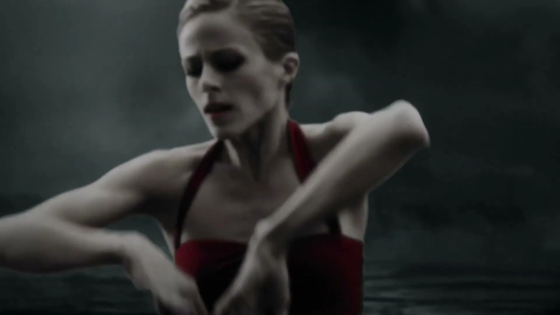A female ballet dancer in a red leotard performs a dramatic routine, moving her arms and legs gracefully against a dark, stormy background.