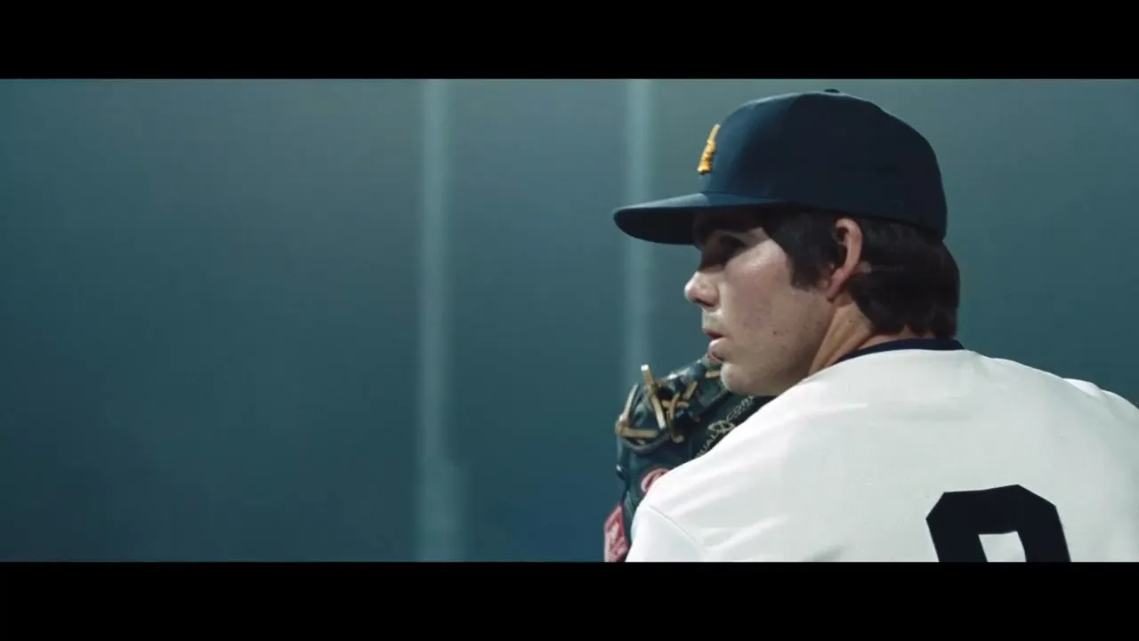 A male baseball player in a white jersey with number 9 and a dark blue cap turns to face the camera on a baseball field at night.