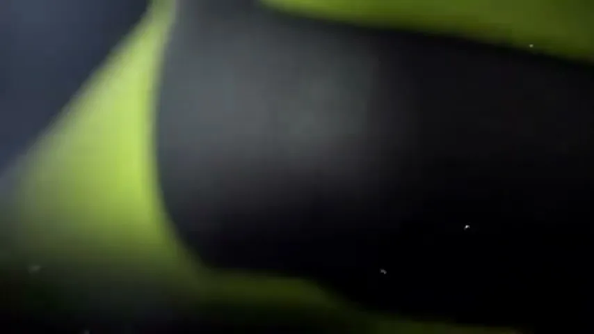 A blurry, extreme closeup shot of a neon green soccer cleat, with water droplets visible against a dark background.