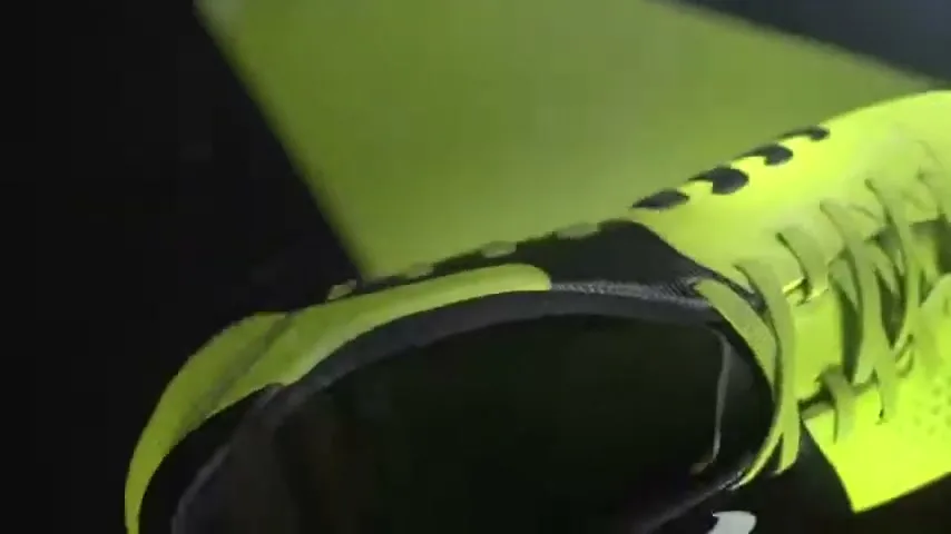 A bright yellow and black Nike soccer shoe is shown in a studio setting, with a reflective geometric object above it.