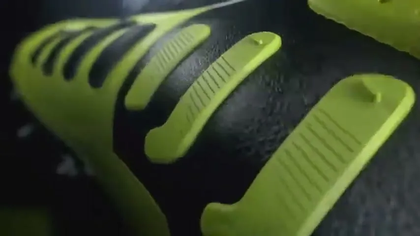 A close-up shot of a black and neon green soccer cleat, highlighting its textured surface and design details in a studio setting.