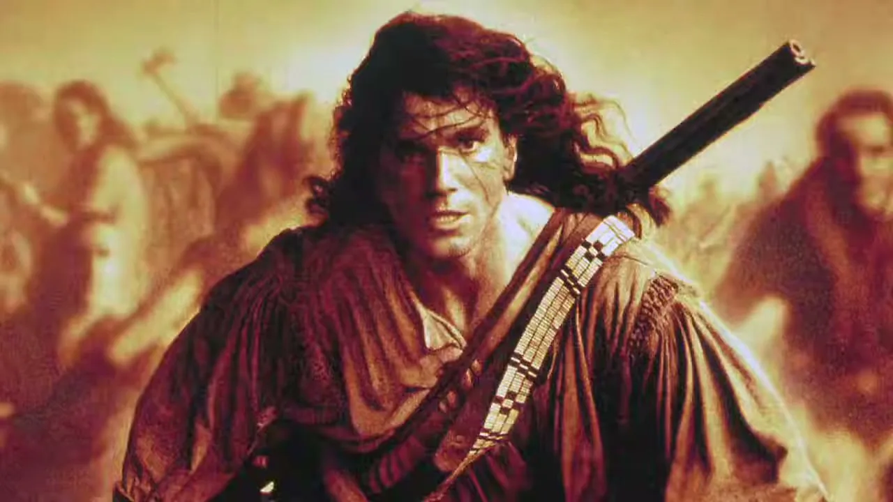 A man with long, dark, curly hair and a rifle slung over his shoulder looks intensely at the camera, with other people in the background.
