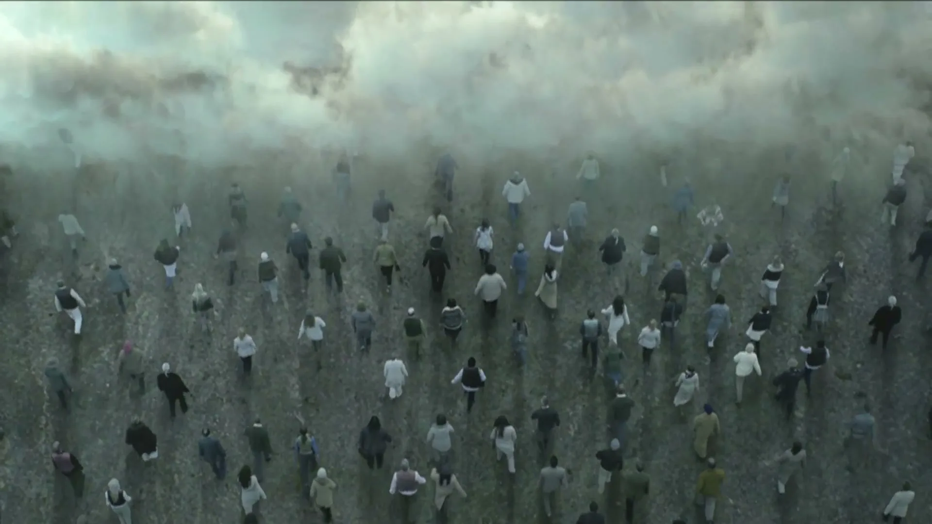 A large crowd of diverse people, dressed in various casual clothes, walk together through a misty, barren landscape under an overcast sky.