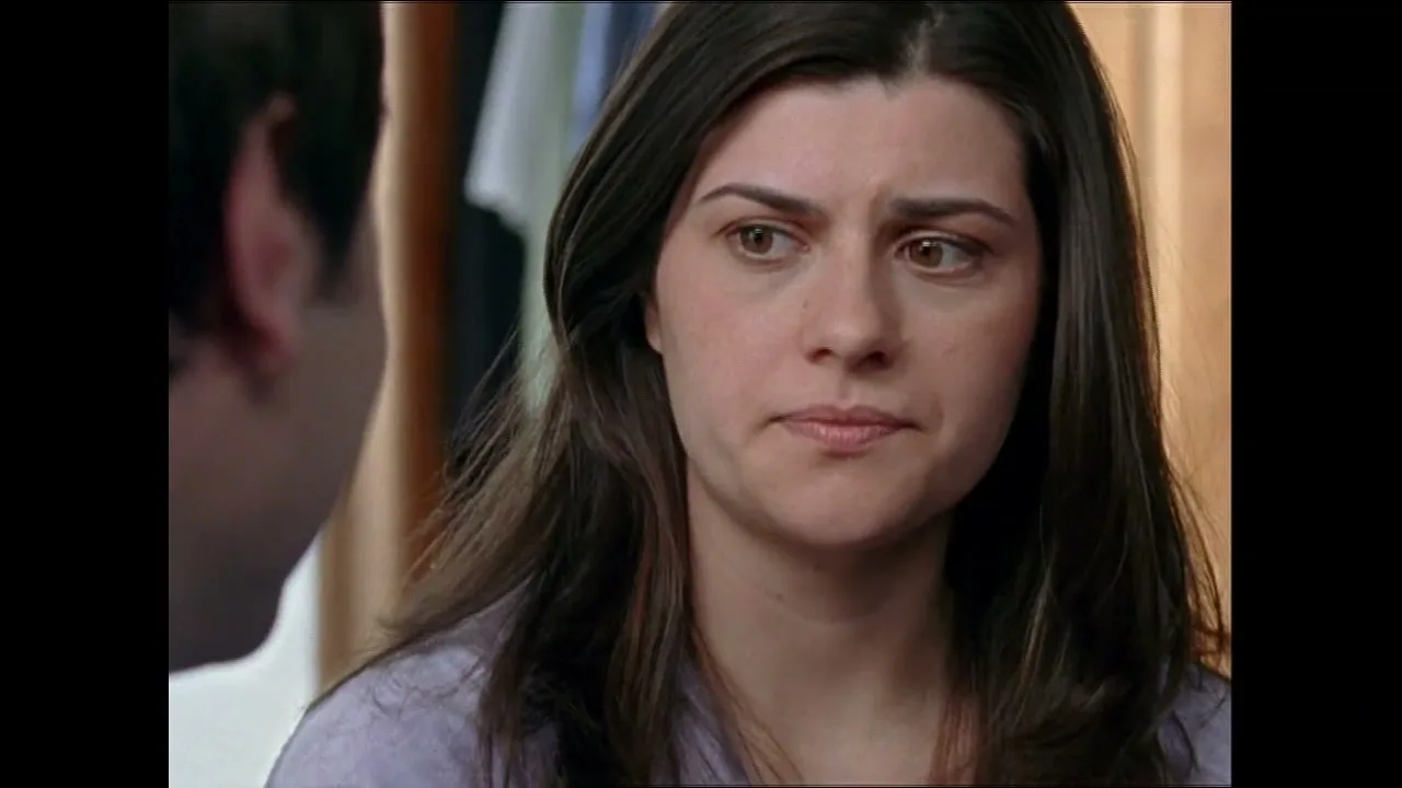 A woman with long dark hair looks at a man with a concerned expression in a bedroom.