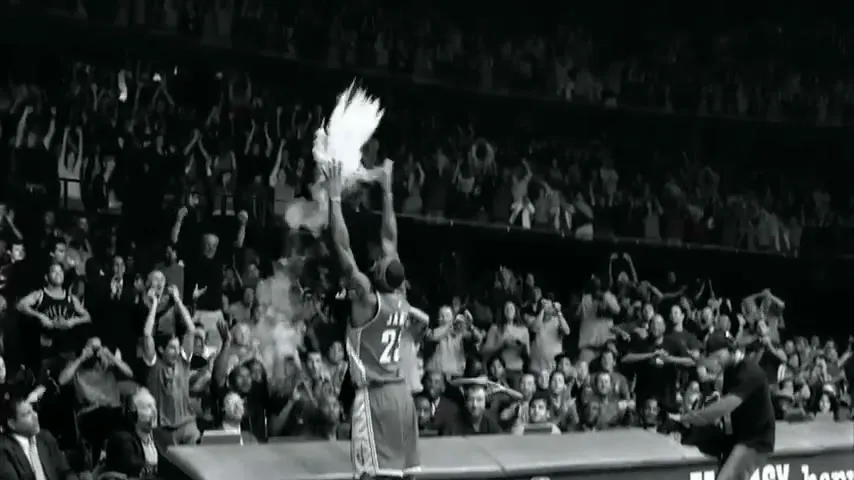 LeBron James, wearing a basketball jersey, throws chalk into the air on a basketball court, with a cheering crowd in the background.