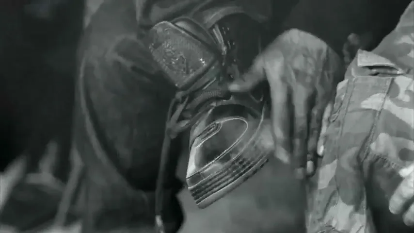 A person's hands are seen dusting off a black and white Nike shoe, with a camouflage jacket visible next to it.