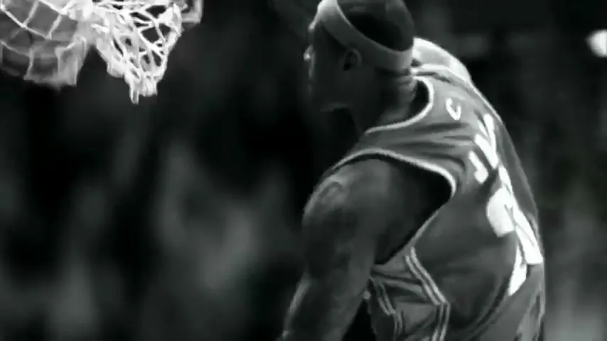 A male basketball player in a jersey with the number 23 dunks a basketball in a black and white shot.
