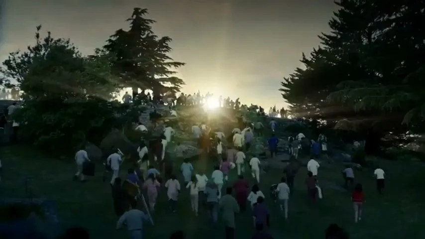 A diverse crowd of people, dressed in various casual clothes, run up a grassy hill towards a bright sunrise in a wide shot.