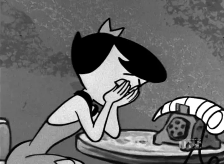 Pebbles Flintstone, a young animated girl with dark hair, covers her mouth in shock while looking at a ram's horn telephone in a cave interior.