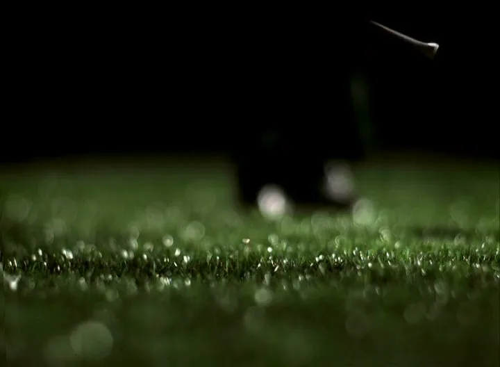 A golf tee flies through the air after being hit, with a blurred green golf course in the foreground and a dark background.