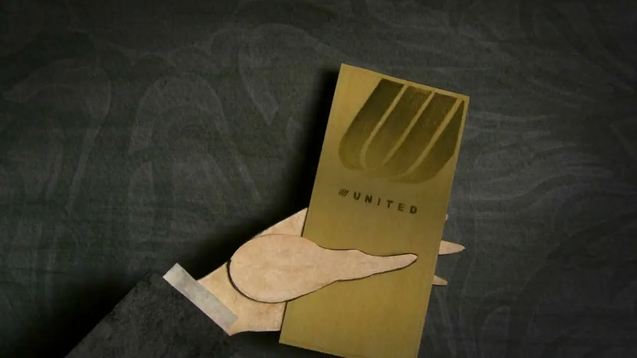 A stylized paper cutout hand reaches for a golden United Airlines ticket on a dark, textured surface, then pulls it away.