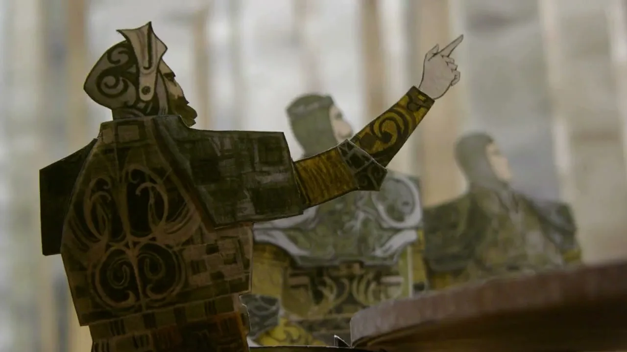 A paper cutout of a male warrior in ornate armor points his finger, with other warriors in the background, in a stylized setting.