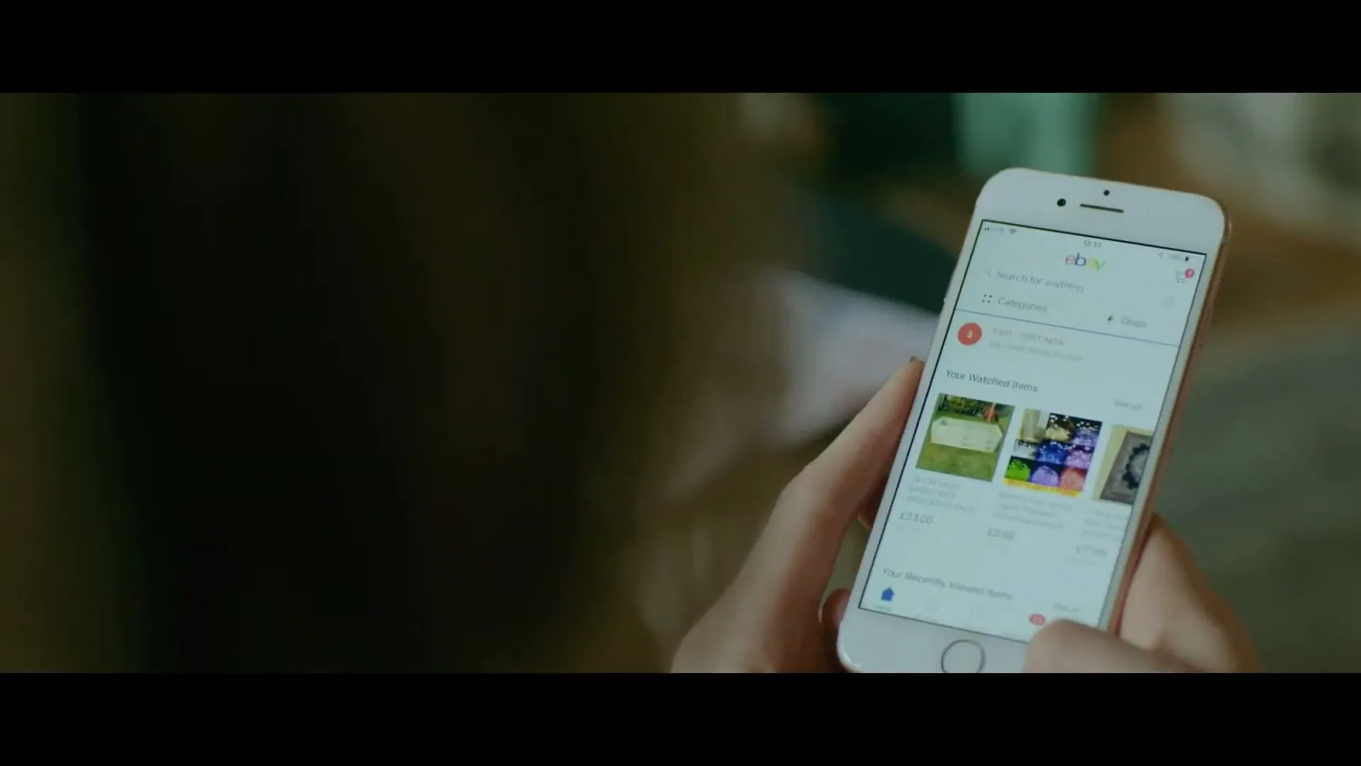 A person's hands hold a white smartphone, scrolling through the eBay app, with a blurred background.