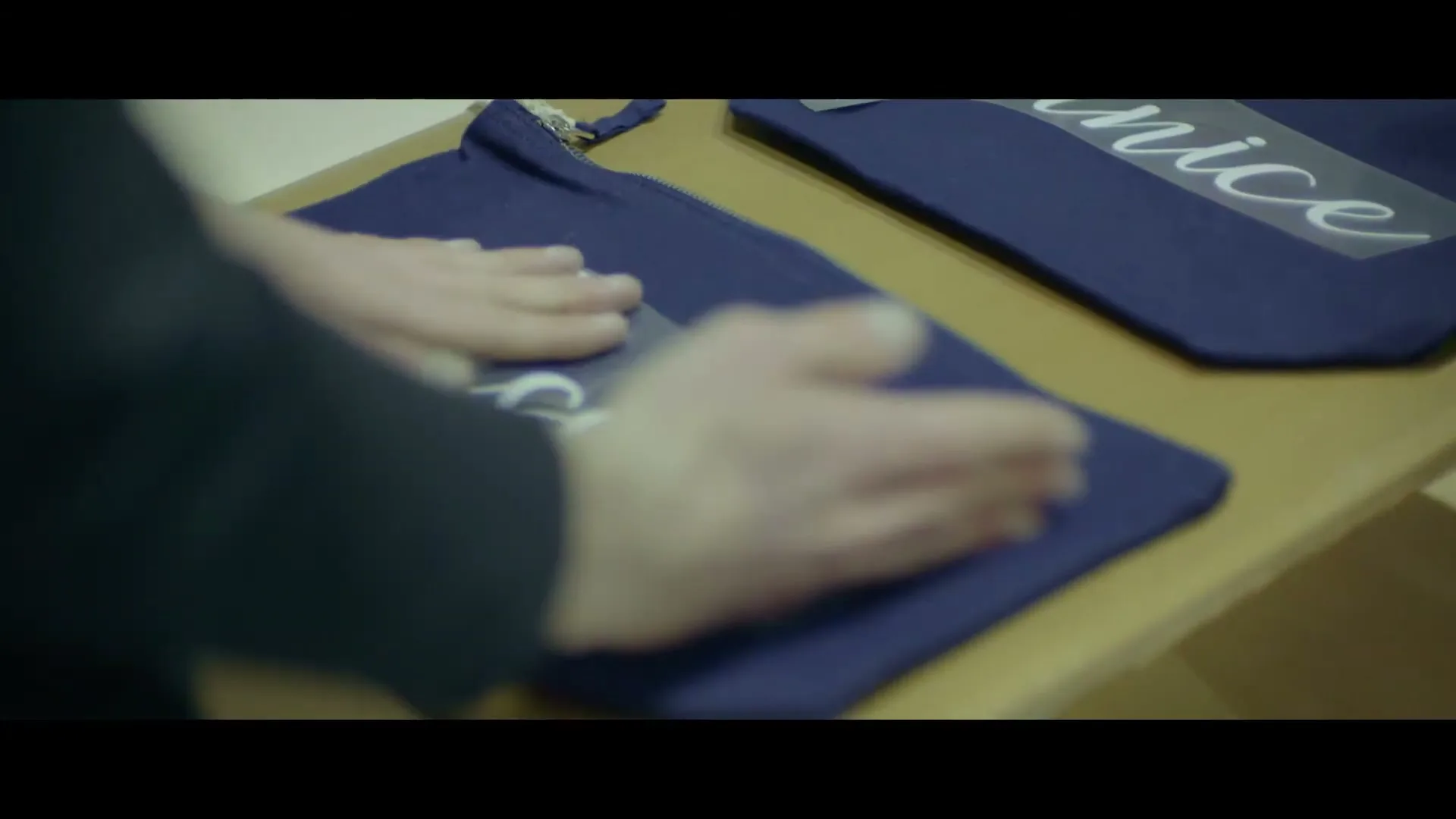 A person's hands carefully apply a white iron-on name, "Jessica", to a small navy blue fabric pouch on a wooden surface.