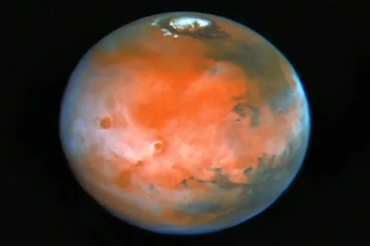 A full shot of the planet Mars, with its distinctive red and orange hues, slowly rotates against a black, starry background.