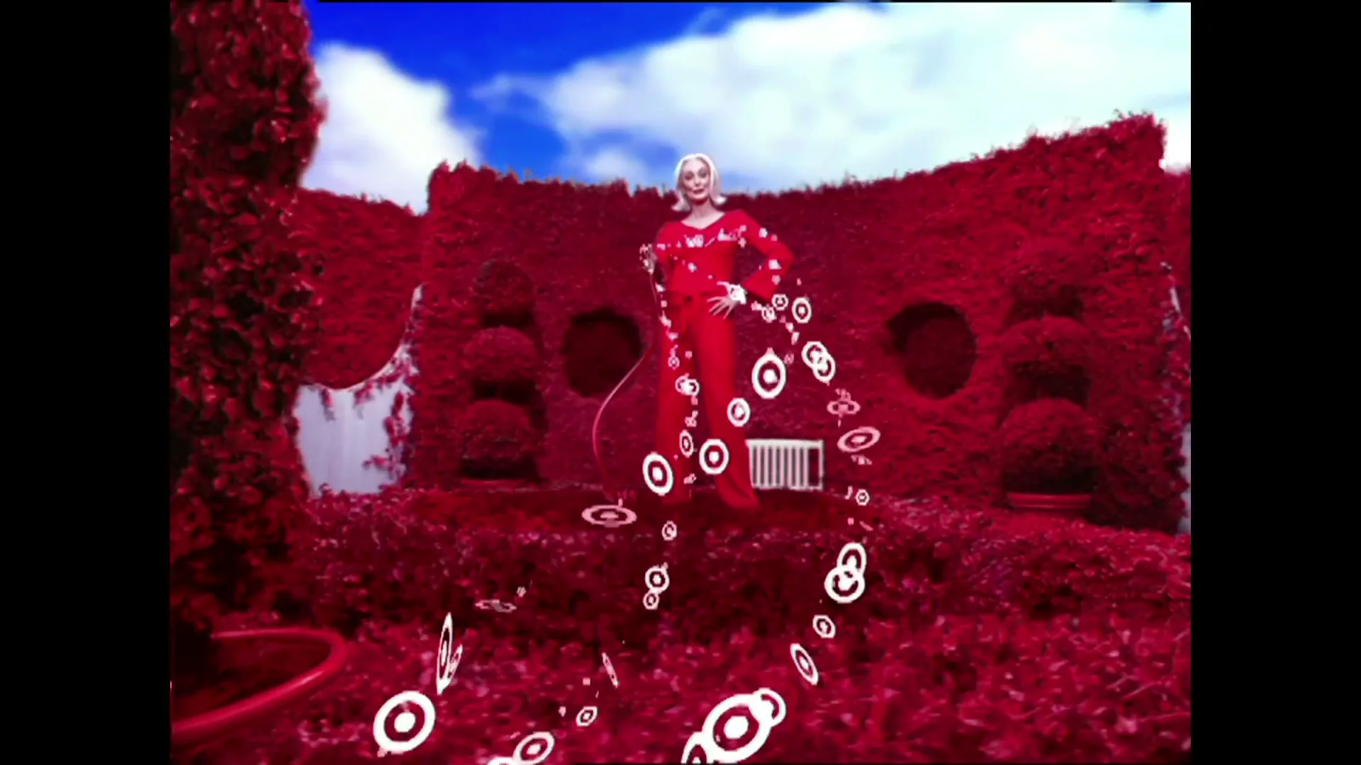 A blonde woman in a red outfit stands in a red topiary garden, with white Target bullseye logos floating around her.