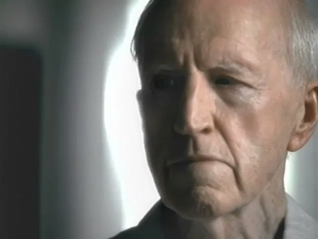 An elderly man with white hair and a light shirt looks off-camera in a softly lit interior.