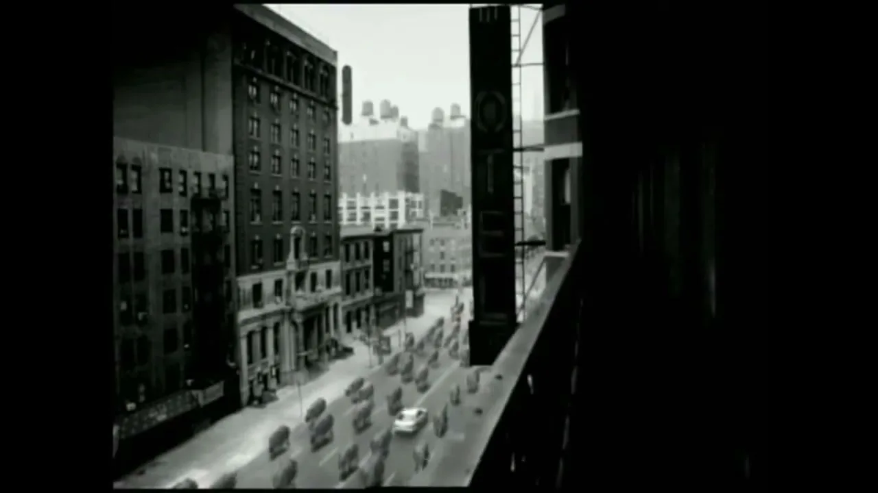A black and white shot from a high-rise window shows a city street with a white car driving through a herd of rhinos.