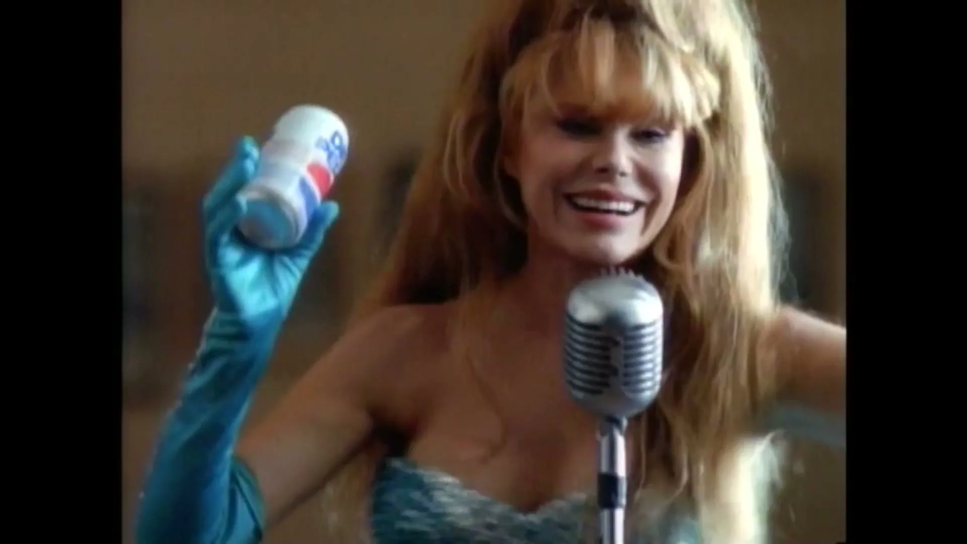 A blonde woman in a blue sequined top and gloves holds a Pepsi can and sings into a vintage microphone, smiling and then screaming.