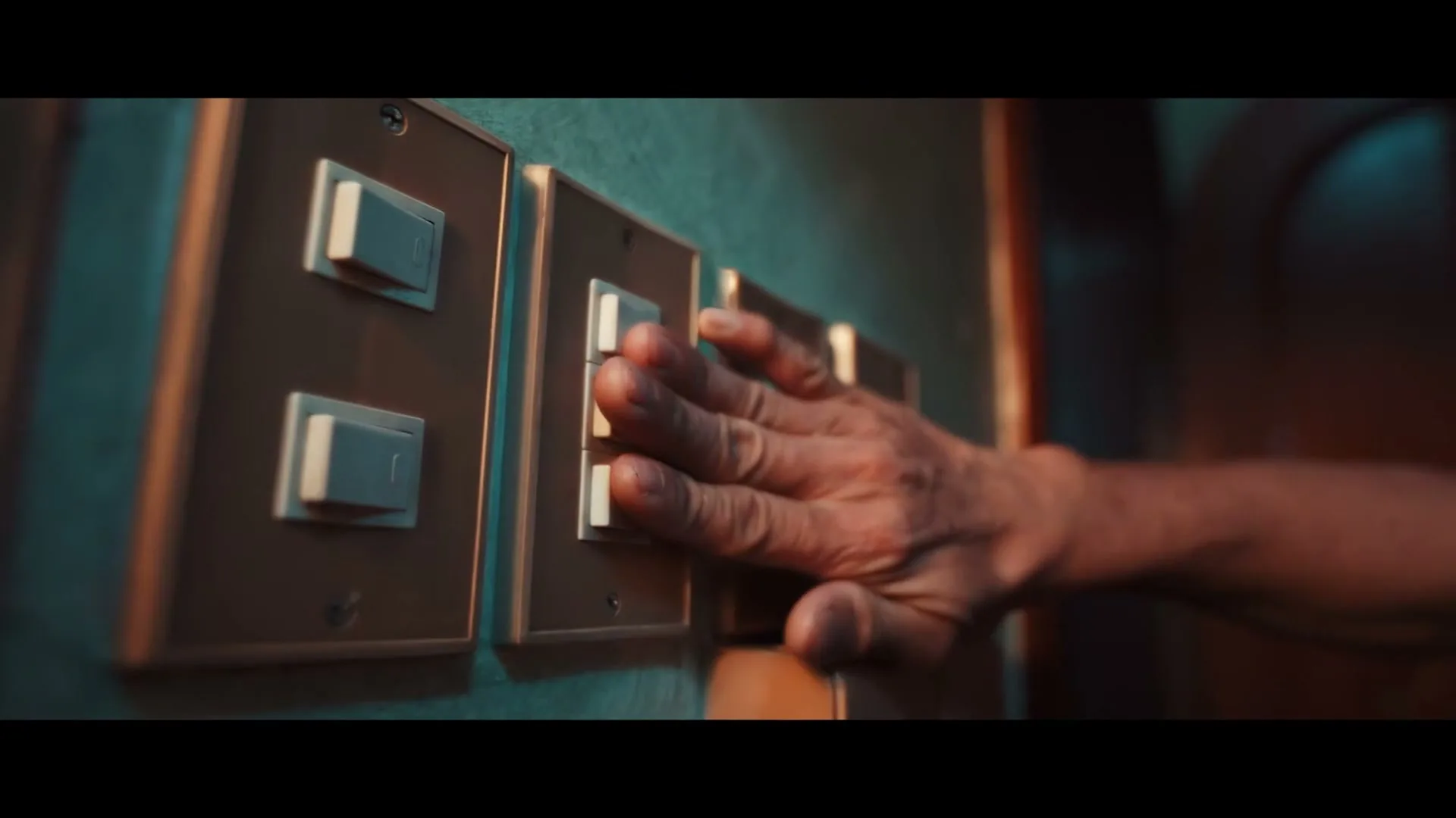 A person's hand quickly slides across a row of light switches, turning them on in a dimly lit room.