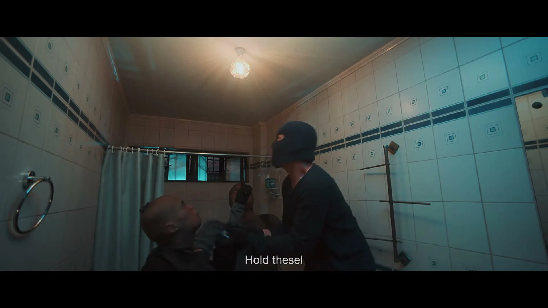 Three men, two in black balaclavas, are in a tiled bathroom; one man in a balaclava hands something to another man, then reaches up to unscrew a lightbulb.