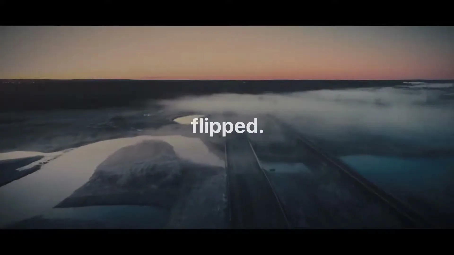 An aerial shot shows a highway cutting through a misty, watery landscape at dusk, with text appearing on screen.