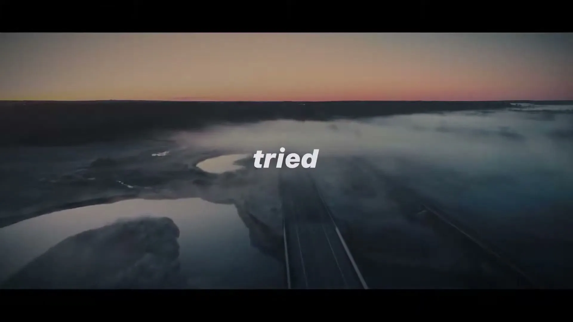 An aerial shot captures a bridge over a river, shrouded in mist, at dawn, with text overlayed on the screen.